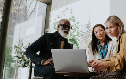 Three employees analyzing information together on a laptop.