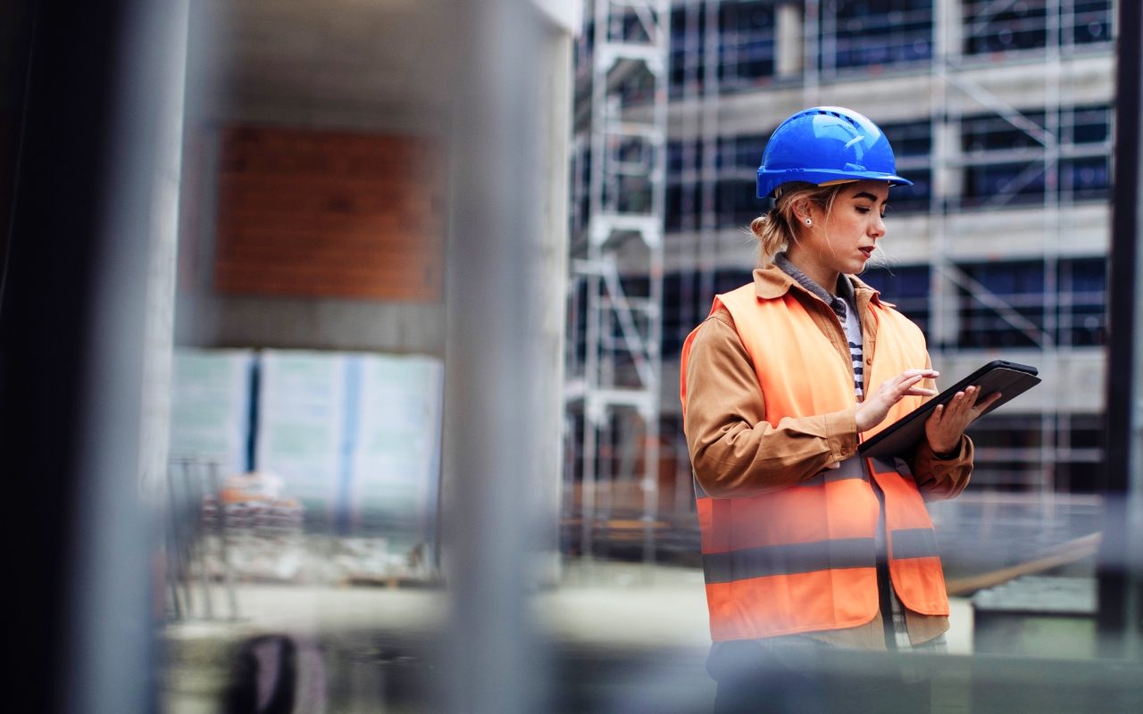 A occupational safety professional with a blue helmet, using an EHS app on a tablet